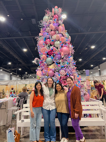 four residents standing in front of a large, pastel-themes Christmas tree at Mistletoe Marketplace
